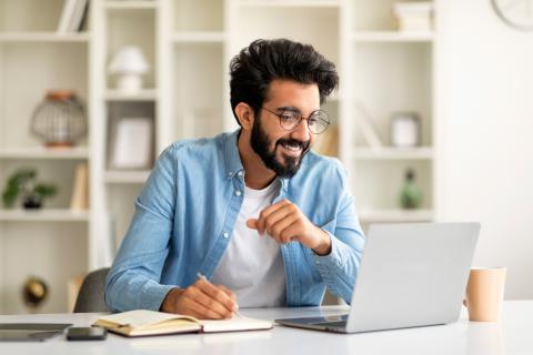 A smiling man makes notes from his laptop