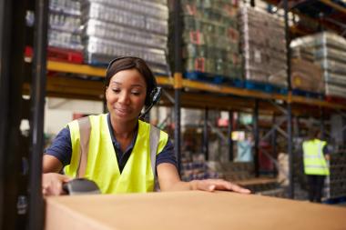 A woman in a high-vis jacket scans stock in a large warehouse