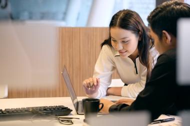 Two women look at a laptop in a office.