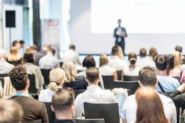 An audience looks at a man talking onstage at a conference. 