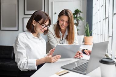 Two smiling women look at a tablet in an office