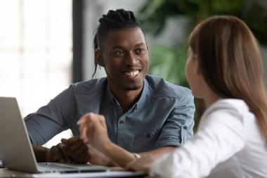 A happy man and woman talk whilst working at a laptop